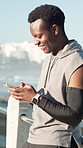Fitness, man and happy with phone outdoor for text message, workout app and running break. Athlete, black person and smartphone on promenade for status update, chat and exercise post on social media