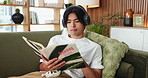 Man, student and reading book in home with headphones, learning and listen to music in living room. Person, literature and research for sustainability, streaming and education with audio at apartment