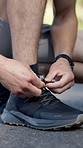 Person, hands and tying with shoes for fitness, workout preparation or running safety on road. Closeup, active or runner getting ready with sneakers or laces for sprint, race or training on asphalt