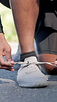 Person, hands and tying with sneakers for fitness, workout preparation or running safety on road. Closeup, active or runner getting ready with shoes or laces for sprint, race or training on asphalt