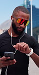 Fitness, earphones and black man in city, smartphone for social media and smart watch. Outdoor, person and runner with cellphone, calm or listening to music, exercise or digital app to track progress