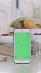 Phone, green screen and home with fruit for telehealth, diet app or menu advertising. Mobile smartphone, display or chromakey with UI, natural organic food or vegetables in kitchen for mockup space