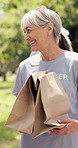 Old woman, volunteer or charity in park with package, conversation or donation for nonprofit service. Senior person, parcel and walk outdoor with NGO group, outreach support or social responsibility.
