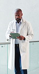 Black man, surgeon and reading with tablet in hospital for research, medical report and test results. Mature doctor, walking and digital for healthcare agenda, treatment planning and surgery feedback