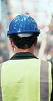 Construction, walking and back of person in warehouse for inventory, supply chain and distribution. Factory, manufacturing and man with safety helmet for shipping, logistics and wholesale supplier