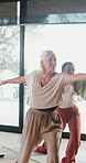 Old woman, warrior pose and smile at yoga class at gym, breathing exercise and wellness at club. Senior person, zen and stretching with group, holistic fitness or happy with mindfulness at studio