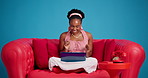 Woman, online and excited with laptop, studio and positive reviews on social media and video on web. Blue background, happy and black person with tech for content creation and influencer on couch