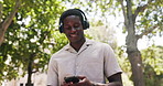 Happy, black man and listening with headphones in park for music, audio streaming or playlist. Male person, relax and comfort with mobile smartphone or sound app for song or entertainment in nature