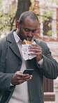 Typing, phone or businessman in town with sandwich, agenda change or online conversation during lunch break. Eating, chat or employee with tech, schedule update or digital communication in free time.