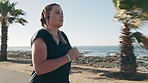 Woman, fitness and running with earphones on beach promenade for workout or exercise. Active, female person or runner with sprint or race for cardio training, health or wellness by ocean coast or sea
