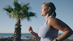 Woman, fitness and running with earphones or music on ocean coast or promenade for outdoor workout. Active, female person or runner with sprint or exercise for cardio training, health or wellness