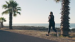 Athlete, woman and running for fitness at beach with exercise, training and cardio challenge. Back, person and workout with earphones for endurance, lose weight and wellness performance on promenade