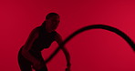 Training, woman and battle rope in studio for fitness, strength workout and cardio on red background. Exercise, strong and person with equipment for muscle development, endurance or power with health