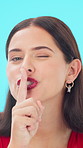 Secrets, face and woman in studio with winking, mystery or whisper in surprise announcement. Silent, gossip or person on blue background with hand gesture, confidential or shush emoji in disclosure.