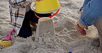 Sandcastle, bucket and hands with family at beach for bonding, support and summer vacation. Travel getaway, holiday and plastic toys with people outdoor for games, sand and tropical adventure