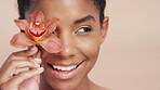 Flower, skincare and black woman with smile, natural cosmetic and antioxidants for antiaging benefits. Happy, person and orchid cover eye for dermatology, wellness and beauty on studio background.