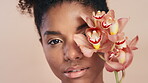 Face, skincare and black woman with flower, beauty aesthetic or antioxidants for antiaging benefits. Happy, female person and orchid plant for dermatology, wellness or self care on studio background.