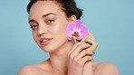 Happy woman, orchid and face for beauty in studio with flower, skincare or petals on blue background. Girl, smile and blossom for sustainable cosmetics, confident or spring for portrait in Spain