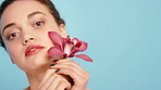Girl, flower and face for skincare in studio with orchid, beauty or petals for texture on blue background. Woman, smile and blossom for sustainable cosmetics, portrait and mock up space in Costa Rica