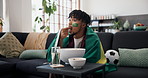 Flag, celebration and man in home, soccer and eating popcorn with happiness, excited and cheering. Apartment, world cup or person on couch, entertainment and sports event for football, snack or goals