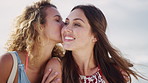 Friends, kiss and women with smile on beach, bonding and laughing at funny joke in nature or outdoor. People, happiness and hangout together on summer vacation, humor and reunion at sea on weekend