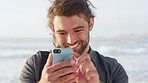 Man, phone and laugh with texting at beach for contact, typing and meme post on vacation in summer. Person, smartphone and smile with mobile app, notification or social network on holiday at seaside