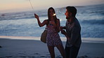Sunset, celebrate and couple with sparklers on beach for holiday, new years eve and summer vacation. Dating, love and happy man with woman with fireworks for travel, bonding and relationship by ocean