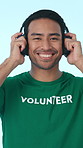 Headphone, volunteer and face of man in studio for charity, outreach and community service with music. Happy, streaming and person with audio, radio and playlist for welfare on blue background