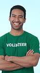 Face, volunteer and man with arms crossed in studio, community service and smile with duty to help. Blue background, ngo and person with confidence for social responsibility, laughing and charity
