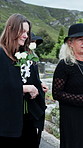 Old woman, group and flowers at cemetery for funeral procession, mourning and loss at ceremony. People, family and floral bouquet with grief, support or respect on walk for memorial at graveyard
