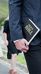 Person, hands and walking with holy bible in cemetery for funeral, word of god or prayer. Priest, family and graveyard with book for burial ceremony, faith or worship in death for memorial service