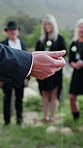 Person, priest and hands with speech in cemetery for funeral, burial or memorial service. Pastor, reverend or speaker talking with family together for grief, condolences or rememberance in graveyard