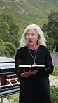 Old woman, reading and bible at funeral outdoor for final prayer, spiritual comfort and religious script. Senior person, talk and holy book for burial service, sacred tradition and farewell memorial