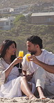 Happy couple, beach and relax with orange juice, cheers or love on sandy shore for romantic date. Man, woman or toast with glasses, drink or beverage for picnic, romance or valentines day vacation