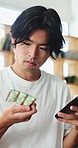 Phone, pills and man in home for healthcare, research information or reading label for dose. Mobile, drugs and Asian person in house for prescription reminder, medical benefits or FAQ with medicine