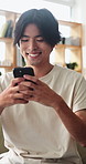 Relax, morning and Asian man on sofa with phone for social media, online dating and connection. Weekend, happy and person on smartphone for reading message, website and notification in living room