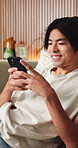 Relax, happy and Asian man on sofa with phone for social media, online dating and connection. Home, scroll and person on smartphone for reading message, website and notification in living room