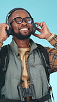 Dancing, hiker and black man with headphones in studio, streaming music and radio for travel holiday. Trekking, listen and happy backpacker with audio tech for playlist, groove and blue background