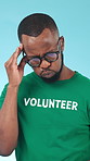 Glasses, headache and stress with volunteer black man in studio for burnout or charity pressure. Breathing, migraine and pain with African person on blue background for activism or welfare tension