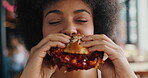 Happy, woman and burger in restaurant with delicious taste, sauce and eating fast food for lunch. Hungry, African person or customer in diner with beef sandwich, take away or meal for unhealthy diet.