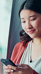 Happy, phone and Asian woman in home with texting, communication or networking on mobile app. Smile, technology and female person with cellphone for contact on website by window in apartment.