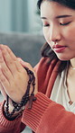 Praying, religion and hands of woman with rosary in home for praise, faith or spiritual wellness. Necklace, gospel and female person with prayer in house for hope, forgiveness or gratitude in house.