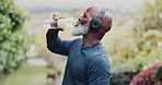 Black man, fitness and drinking water with bottle in nature for hydration, break or rest. Active senior, male person or African runner with mineral liquid, aqua beverage or headphones for recovery