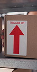 Label, arrow and person with box on shelf in storage depot for delivery, distribution or shipping. Cardboard, package or parcel in empty warehouse for ecommerce, employee and supply chain export