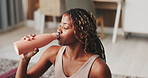 Black woman, drinking water and break for exercise in home on floor, thinking and liquid for hydration. African person, bottle and reflection with fitness, wellness or smile for electrolytes in house