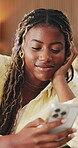 Black woman, phone and smile with typing on home sofa for communication, internet and online dating. Female person, technology and connection to browse on social media app in living room on couch