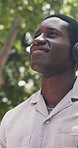 Black man, phone and happy at park with headphones, streaming or listen to music on commute in summer. African person, smile and inspiration with thinking, mobile app or audio subscription in nature