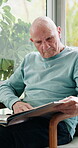 Senior, man and reading a book in home for literature hobby, cognitive stimulation and knowledge. Window, old person and relax with literary fiction in house for learning, information and retirement