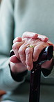 Hands, walking stick and injury in home for retirement with rest, recovery and mobility aid in living room. Senior person with disability, cane and parkinson in lounge with rehabilitation at house