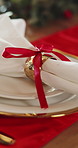 Table, ribbon and Christmas with plate for dining decor, serving preparation or style in home. Empty, cloth and crockery with stylish golden ring for event catering, dinner service or hospitality